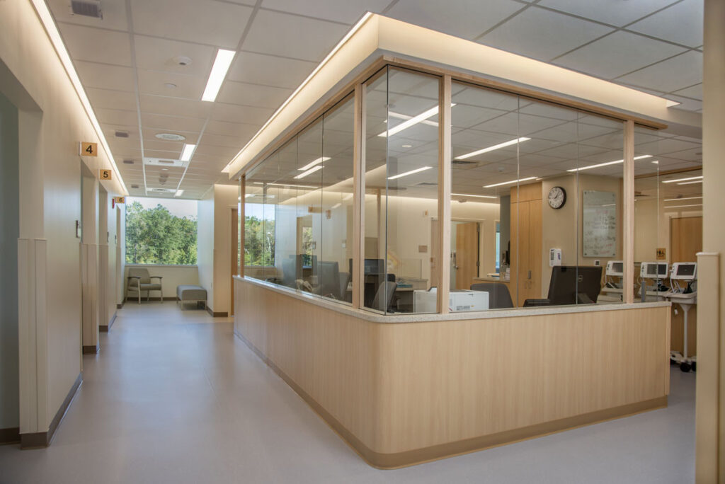 Photo of glass partitions surrounding an infusion bay station with comupters, chairs, and mobile infusion pumps