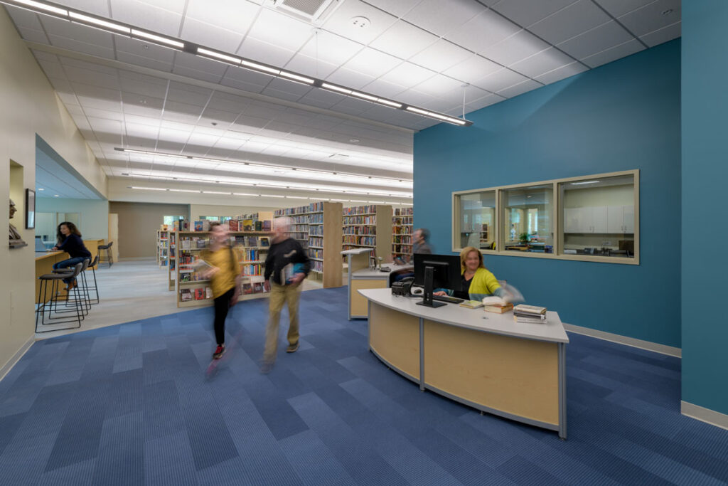Interior circulation desk with librarians and members walking around and sitting at cafe tables
