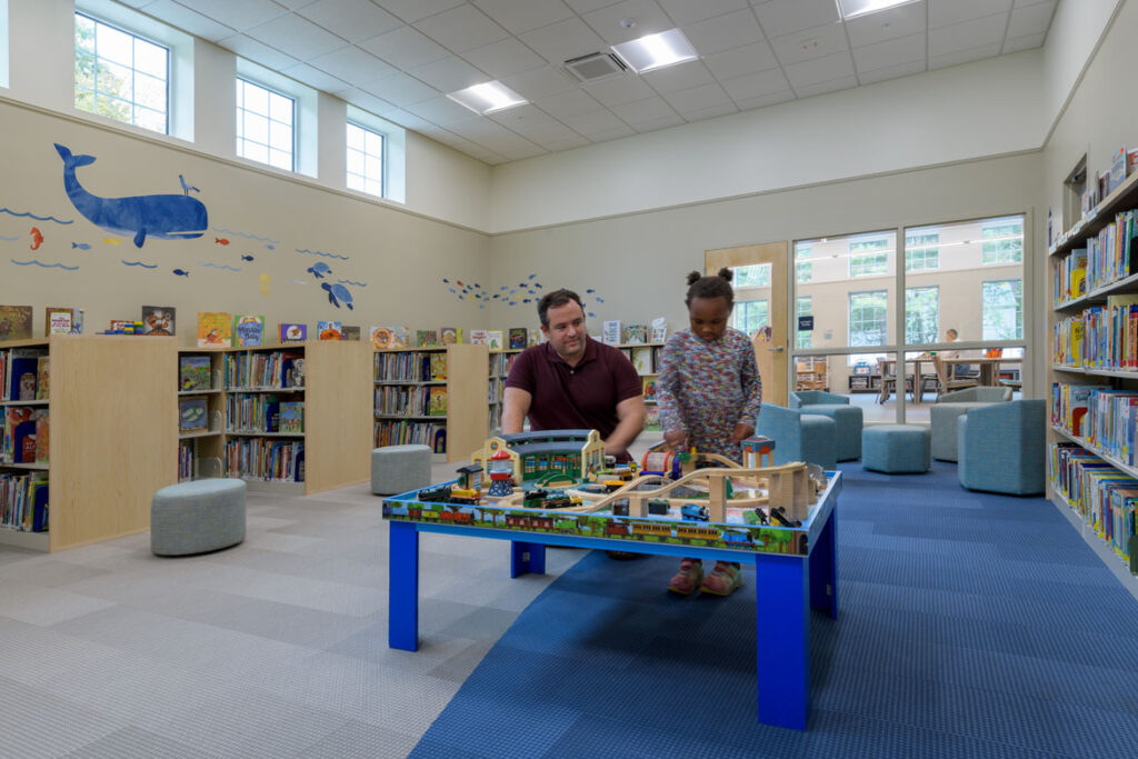 Children's room with book stacks with parent and child using activity table at North Hampton Public Library