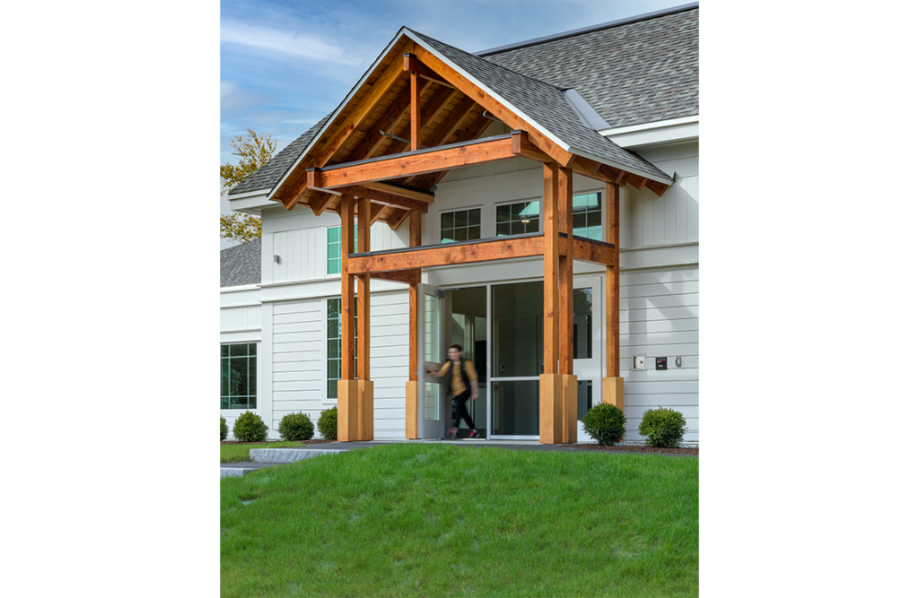 Vertical exterior with a person walking through the doors of North Hampton Public Library in North Hampton, NH.
